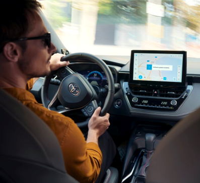 Un homme vêtu d’un pull orange tourne à droite alors qu’il conduit une voiture Toyota. Le système multimédia de la voiture affiche une mise à jour logicielle.