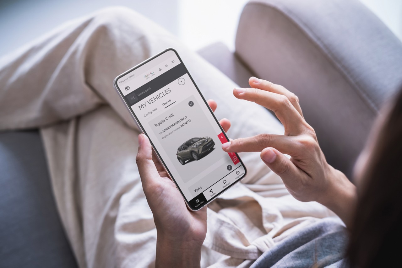 Une femme tape sur l’écran de son smartphone. On y voit un Toyota C-HR sur la page Mes véhicules du site personnel de Toyota.